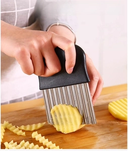Close-up of hand using a stainless steel crinkle cutter to slice wavy potato chips