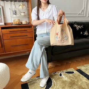Détail du sac en toile beige avec broderie florale et anses à carreaux orange