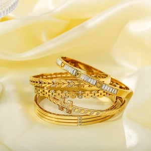 Stackable gold-plated stainless steel bracelets with zircon charms on satin fabric background