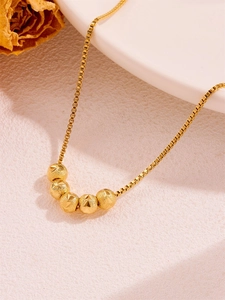 Close-up of gold box chain necklace with five frosted geometric bead pendants