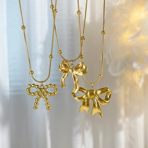 18K gold-plated titanium steel bow necklace with beaded chain on soft white fabric