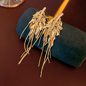 Macro detail of golden wheat leaf earrings with long snake chain tassels on a dark display