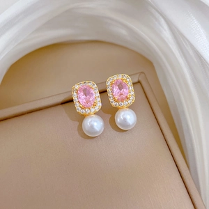 Detailed shot of gold earrings with pink zircon and white pearl on beige leather tray