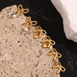 Detail of 18K gold-plated bow earrings with white pearl and gold heart pendants