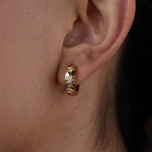 Gold star huggie earrings with cubic zirconia stones worn on ear for a luxury look