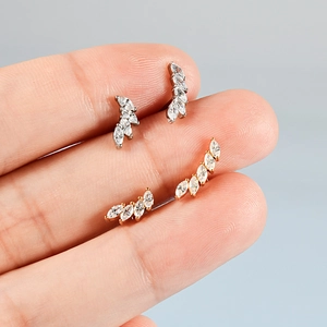 Clous d'oreilles incurvés en argent et or avec zircons marquises tenus entre les doigts