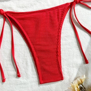 Detail of red textured bikini bottom with side ties and waffle fabric on white textile