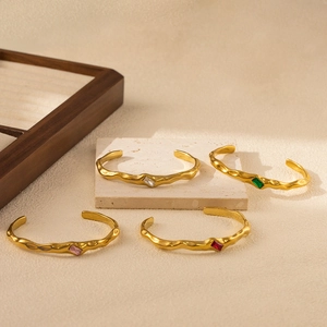 Close-up of wavy gold stainless steel C-shape bangles with colorful rectangular zircons