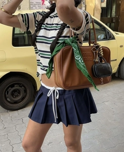 Dettaglio borsa in pelle marrone con logo, sciarpa paisley e mini charm su polo a righe
