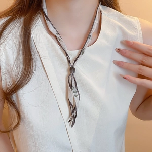Close-up of elegant scarf necklace with beige paisley fabric and dark accent slider