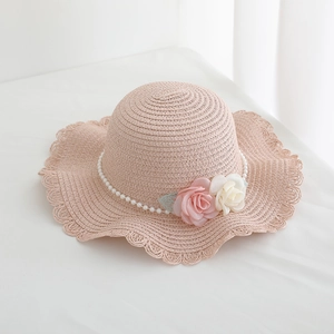 Detailed texture of pink straw sun hat with pearl chain and fabric floral accents