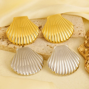 Detailed view of gold and silver shell earrings on stone with yellow silk backdrop