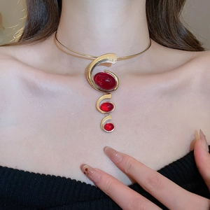 Detail of a gold choker necklace featuring three red oval resin stones on a model