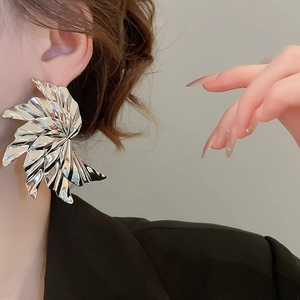 Close-up of oversized silver textured metallic earrings with a stylish wrinkled surface