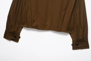 Detail of pleated hem and buttoned cuff on a dark coffee textured long sleeve jacket
