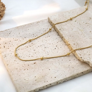 Detail of 18k gold snake chain necklace with beads on a beige stone and silk backdrop