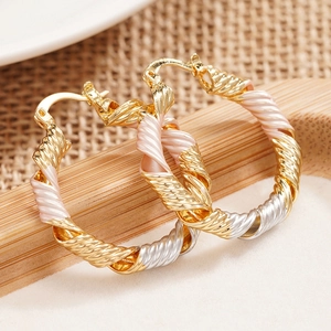 Three-color twisted hoop earrings in gold silver and rose gold on a wooden display stand