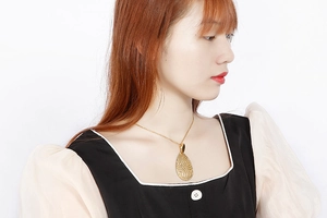 Close-up of a gold teardrop-shaped hollow pendant with intricate filigree on a model