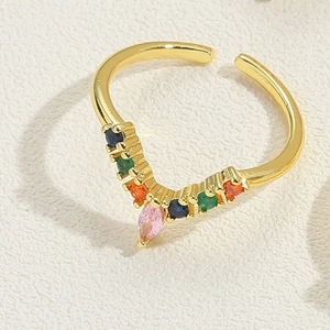Close-up of golden V-shaped adjustable ring with multi-color zircons on white texture