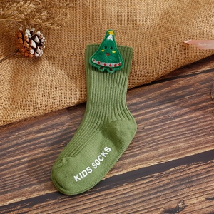 Detail of green Christmas baby sock with 3D tree patch and anti-slip grip on wood background