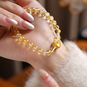 Close-up of yellow citrine bead bracelet with gold heart charm on a model's wrist