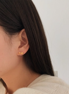 Close-up of a model wearing a delicate gold bow stud earring with a metallic finish