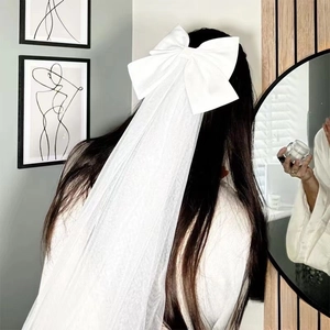 Detail of a white satin bow bridal veil with long tulle layers shown on a model