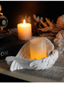 Close-up of white angel wing resin candle holder with a warm yellow pillar candle
