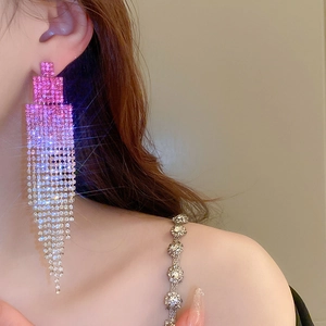 Détail de boucles d'oreilles pendantes à pompon strass dégradé rose et blanc sur mannequin