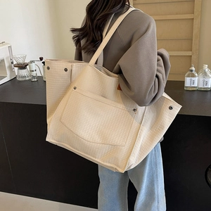 Detail view of large quilted tote bag with front pocket and metal rivets in beige