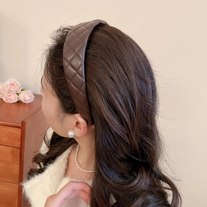 Detail view of wide dark brown quilted leather headband worn by a model in a home setting