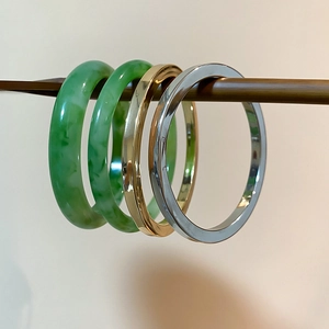 Detail of four resin and metal bangles with green marble texture on wooden stand