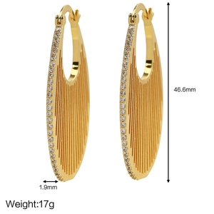 Dettaglio di orecchini a cerchio ovali in oro 18k con trama a costine e zirconi laterali