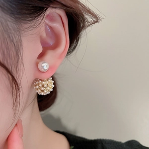 Close-up of elegant gold-plated pearl stud earrings worn with a double-sphere cluster design