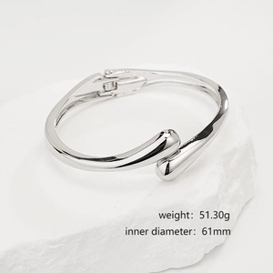 Detail of irregular silver crossover open bangle with polished metallic finish on white stone