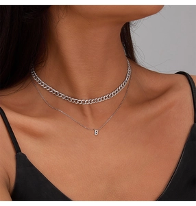 Close-up of stacked silver necklaces featuring a zircon Cuban chain and a B pendant