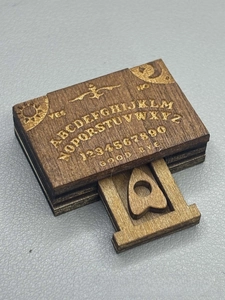 Close-up of a miniature wooden Ouija board box with engraved alphabet and planchette