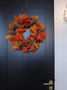 Detail of autumn wreath with faux maple leaves and berries on a dark wooden door