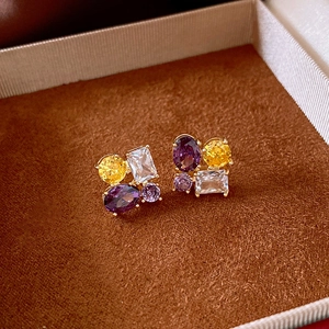 Macro detail of gold-plated oval stud earrings with purple and yellow zircon inlay