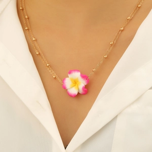 Detail van de bohemien gouden ketting met een levendige frangipani bloem hanger