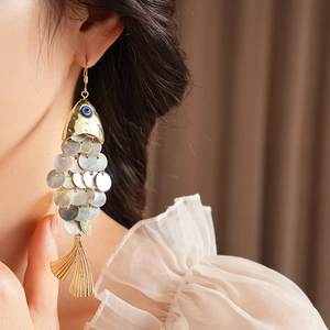 Detail of vintage gold fish earrings with shell scales and blue gem on a female model