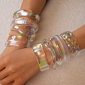 Iridescent acrylic geometric bracelets stacked on wrist against a warm stone backdrop