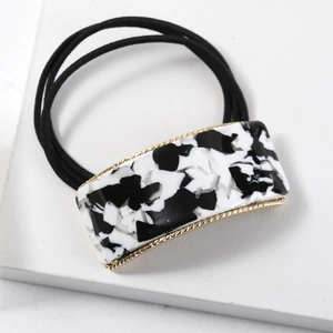 Close-up of marble pattern square buckle on black elastic hair tie with gold metal trim