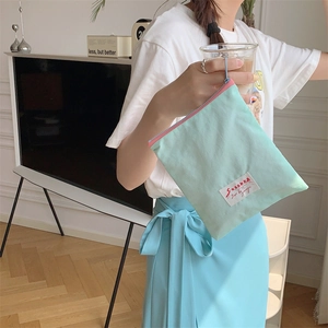 Mint green nylon cosmetic pouch with pink zipper held by a model in a cozy home setting