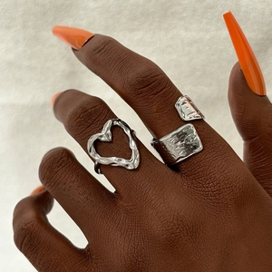 Detail of adjustable silver textured wide band and hollow heart ring on hand