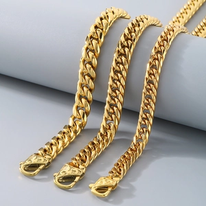 Close-up of golden Cuban links with patterned lobster clasps on grey display stand