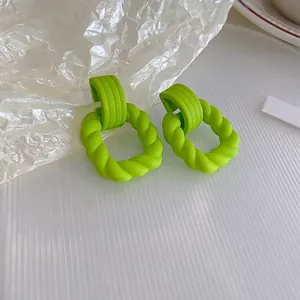 Detail of neon green twist textured hoop earrings on a minimalist white surface