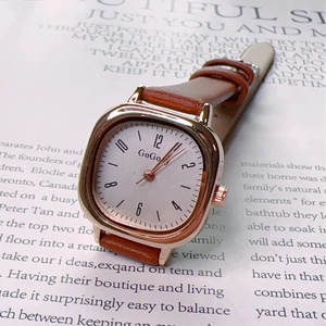 Vintage square quartz watch with rose gold case and brown leather strap on a book
