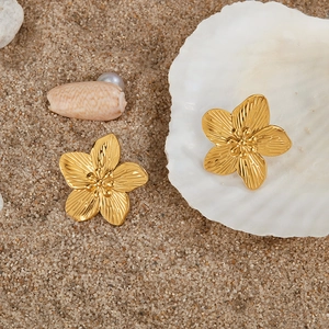 Detail of gold flower earrings with brushed texture on shell tray at beach