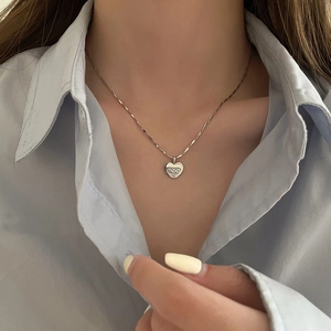 Detail of a silver heart pendant necklace with engraved hearts worn by a model